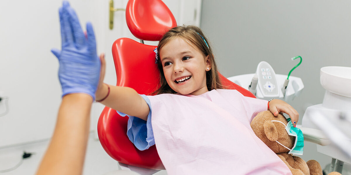 Cute little girl sitting on dental chair and having dental treat