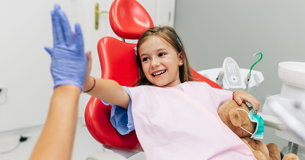 Cute little girl sitting on dental chair and having dental treat